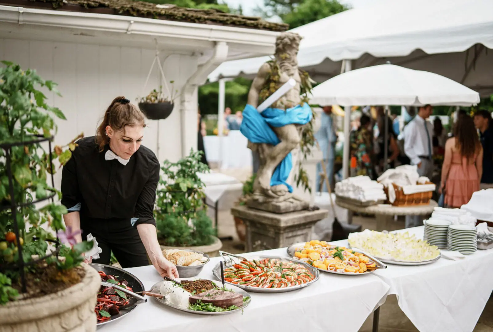 Caterer arranging food at outdoor event table.