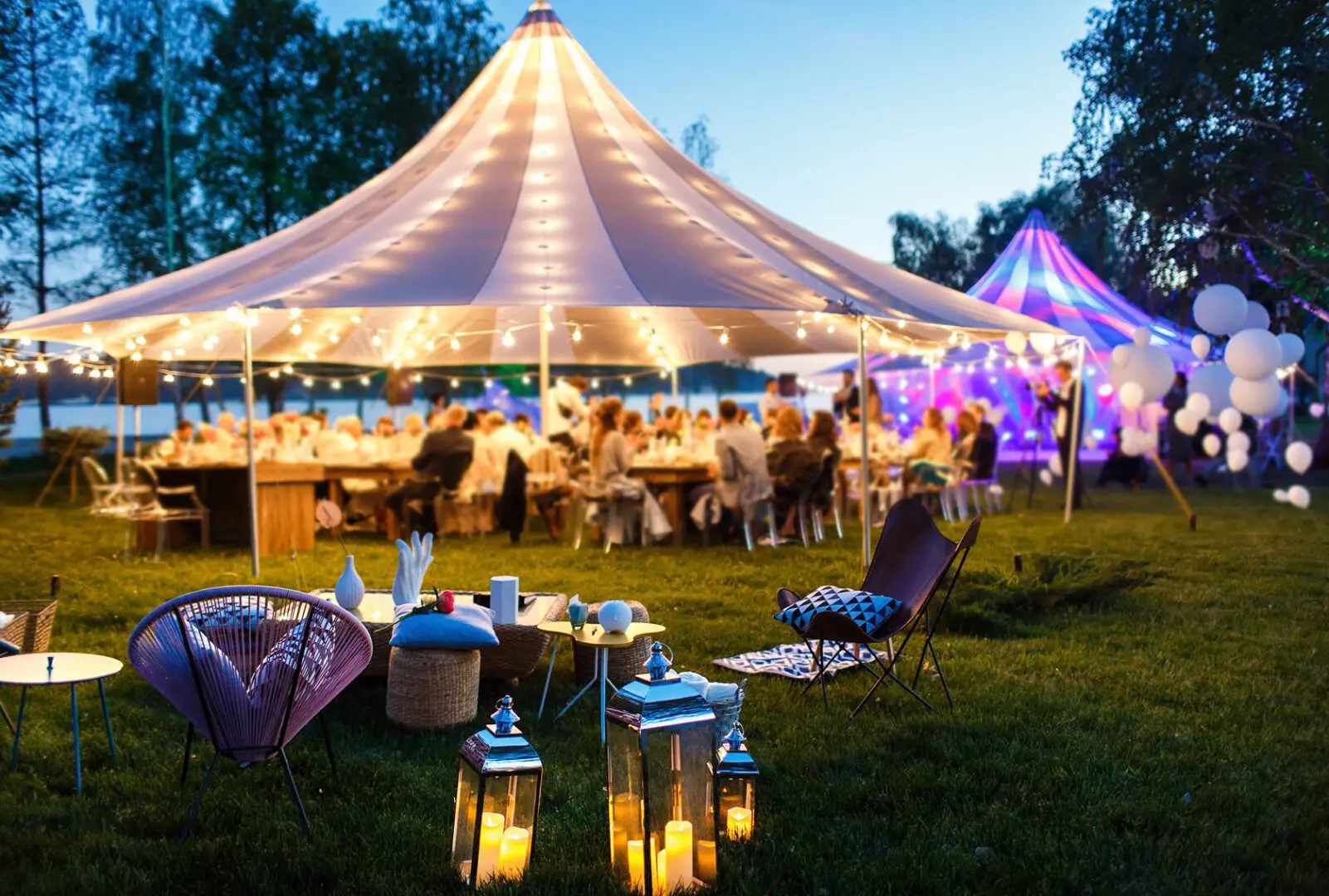 Outdoor party under illuminated tent at dusk.