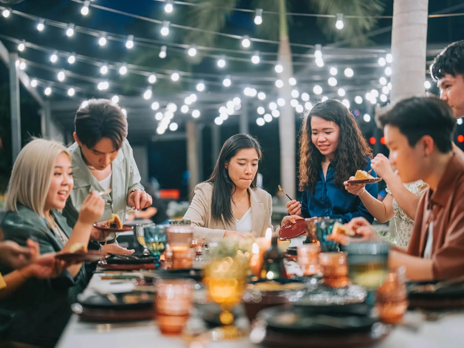 Friends dining outdoors under string lights.